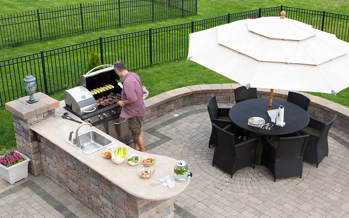 Man grilling on backyard patio in yard with a fence