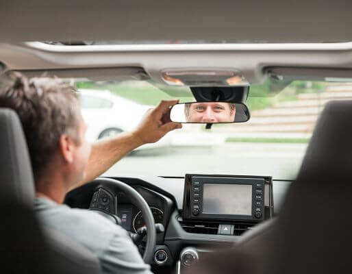 Man in car looking into and adjusting the rear view mirror