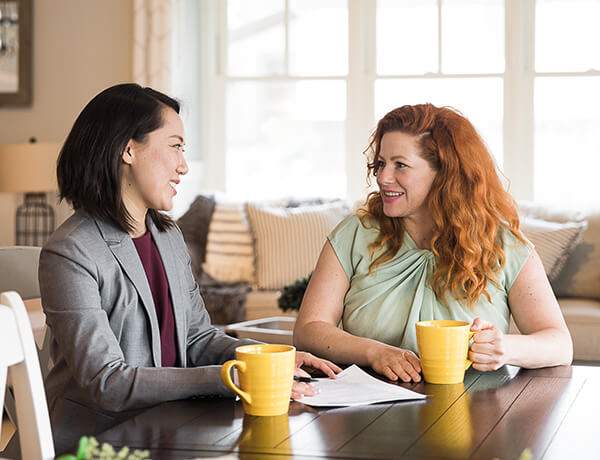 Two women meeting at a table discussing cheap auto insurance.