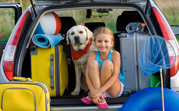 little girl and dog sitting in the back of a packed up car