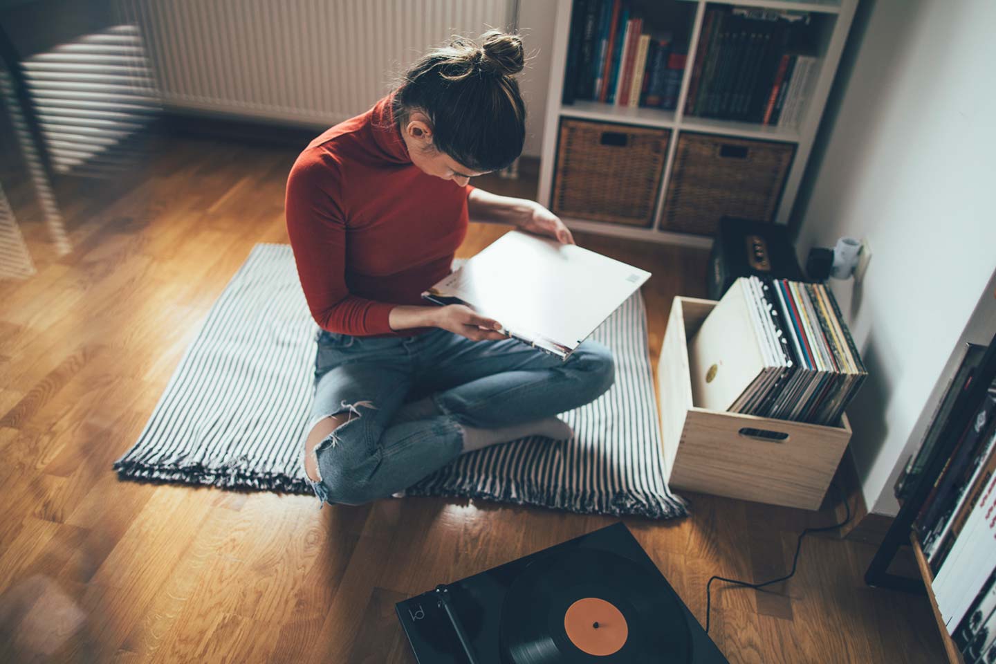 Young woman sitting on floor and listening to her vinyl records collection