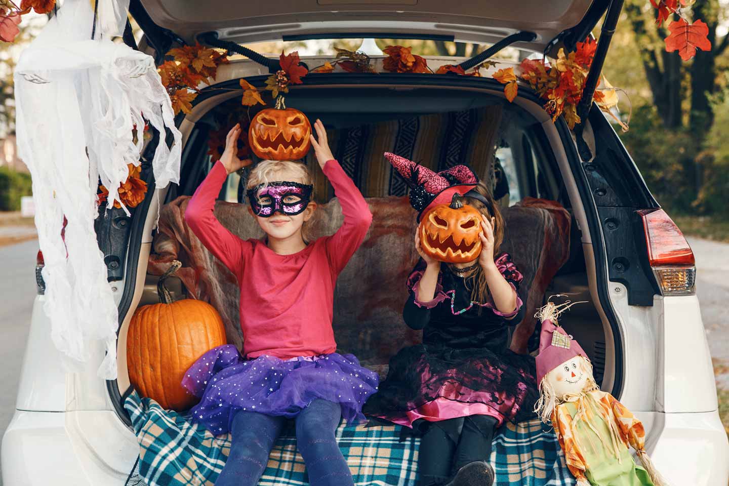 Young sisters celebrating Halloween and sitting in the trunk of a car