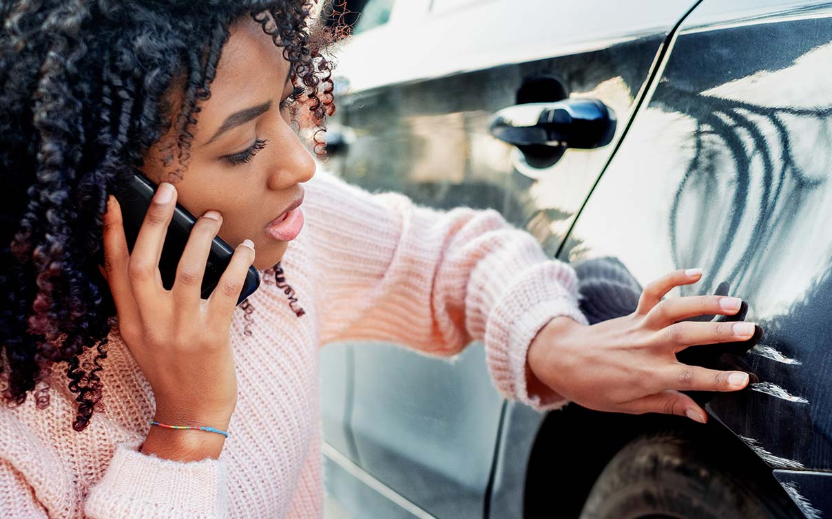 woman on phone inspecting car damage