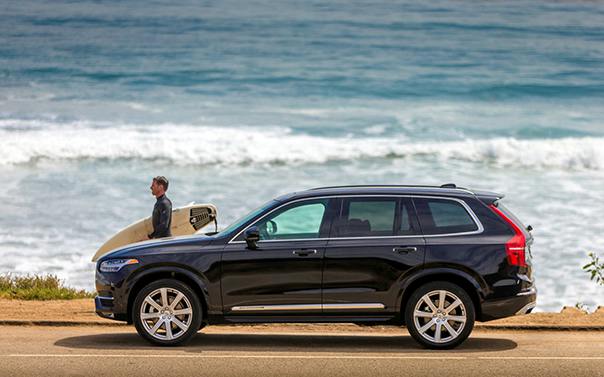 man with surfboard standing next to new volvo suv