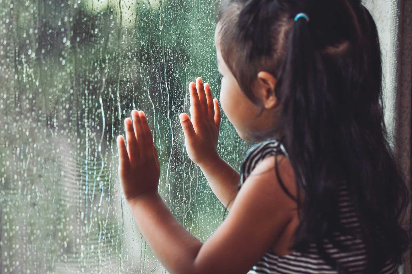 Young girl looking outside through a window on a rainy day
