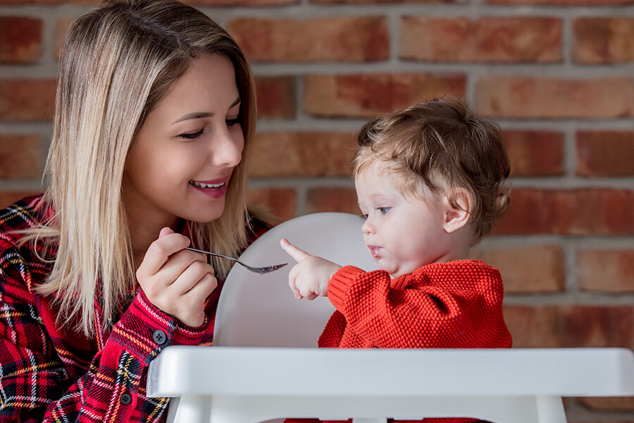 Mother feeding baby food in kitchen