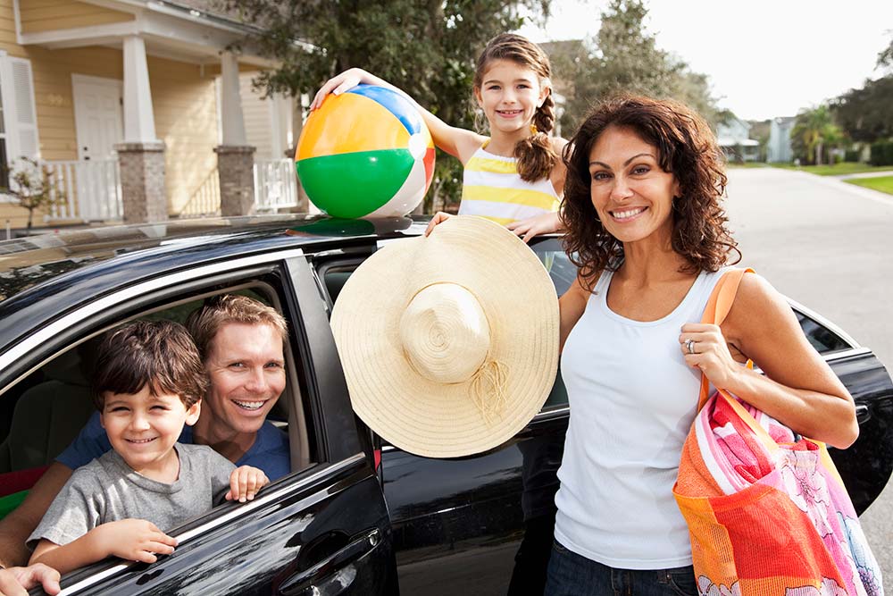 Family standing around car outside their house preparing to go to the beach