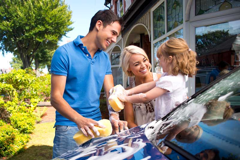 Family happily washing their car in driveway of their home