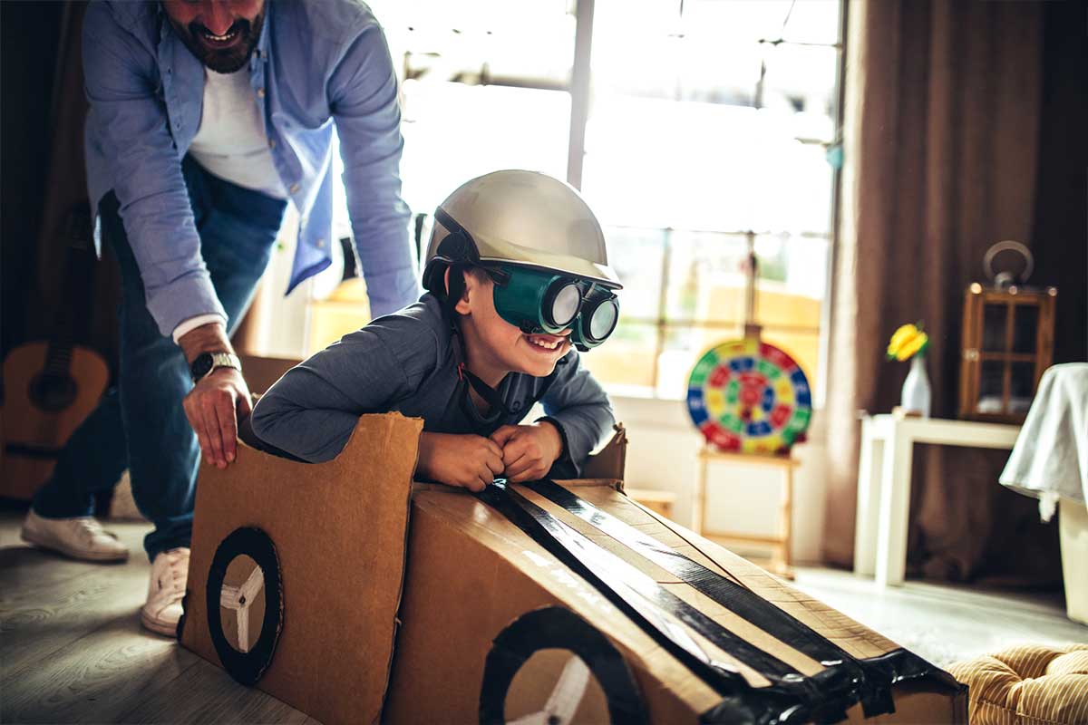 Father and son playing car racing with cardboard boxes