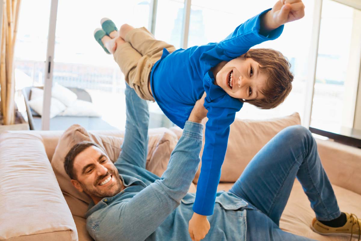 Father and son playing together on sofa in apartment living room