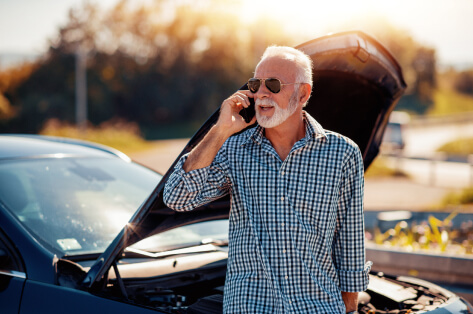 Man on the side of the road leaning against his car with the hood up, calling for automobile help.